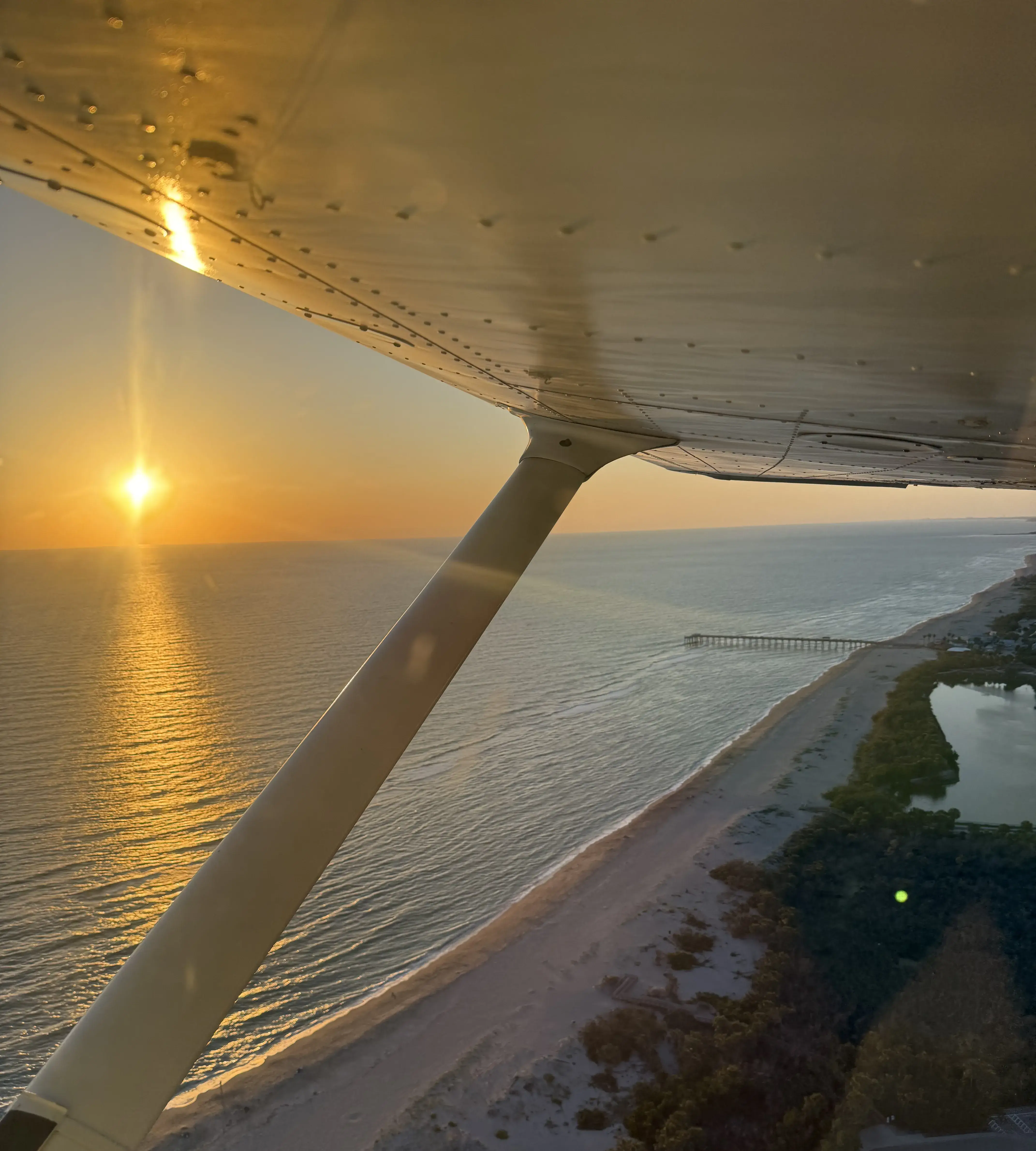 View of the beach from inside an flying airplane with the sunset in the background