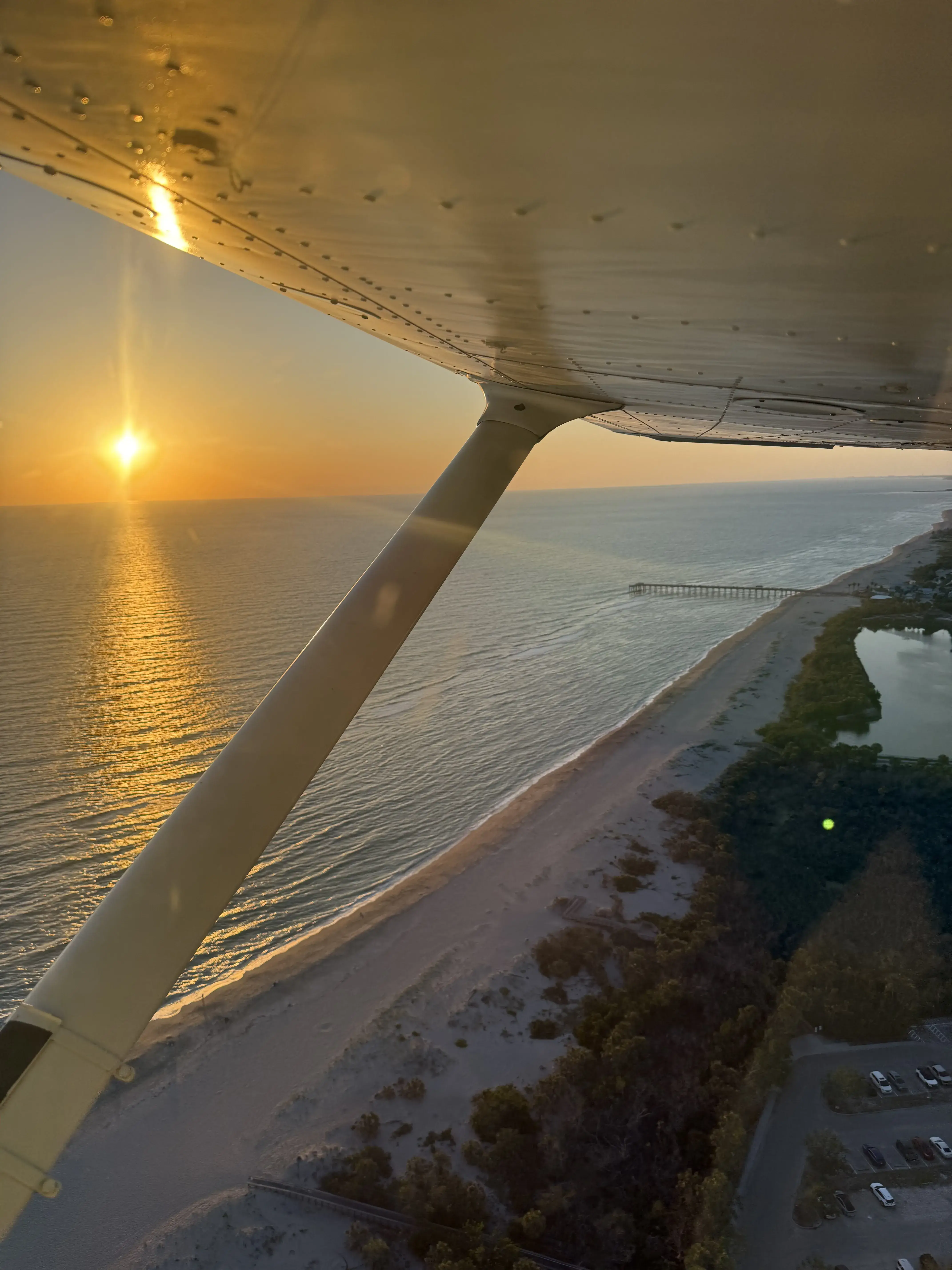 View of a beach with the sunset in the background form a flying airplane window