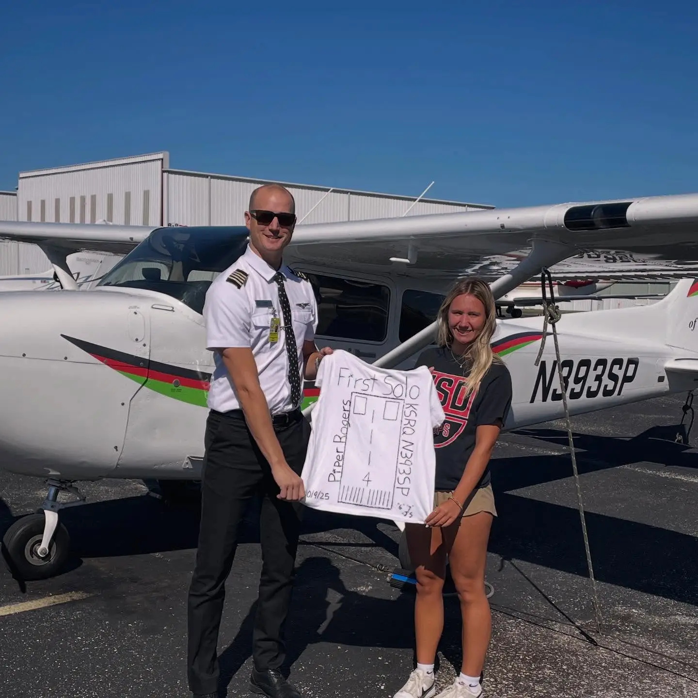 Student and CFI smiling at the camera while holding a shirt saying First Solo