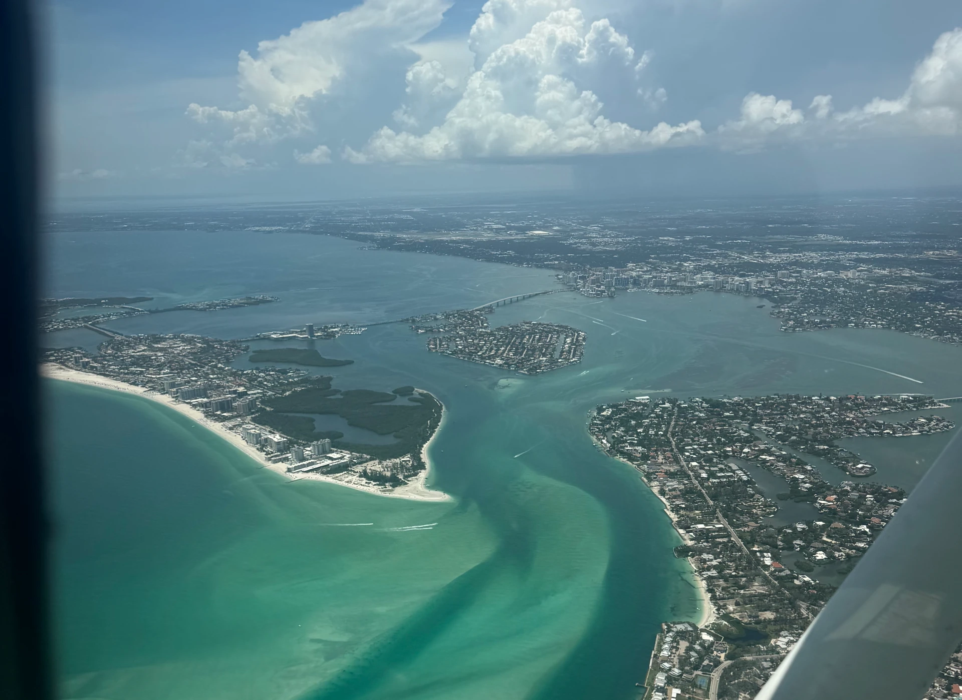 Flight over city and sea seen from plane window inside cockpit during the day