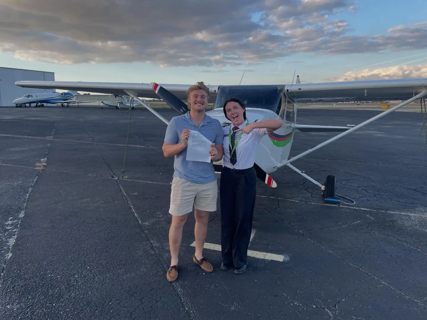 Student and CFI smiling at the camera while holding a certificate in front of a plane