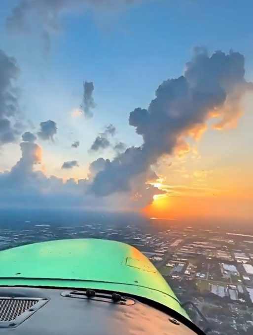 View of the wing of an airplane and the city below during flight. Clouds and sun in the background