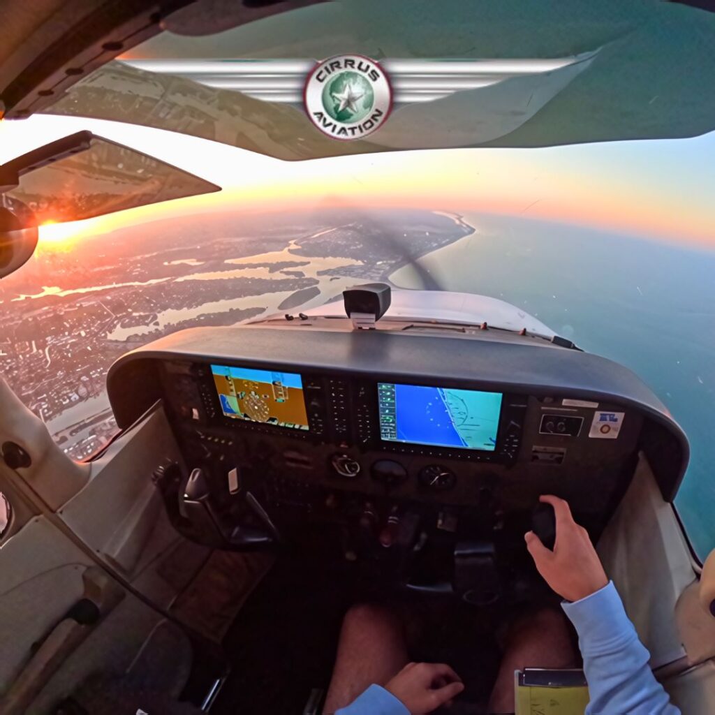Airplane cockpit during flight with the sunset in the background and Cirrus Aviation's logo at the top