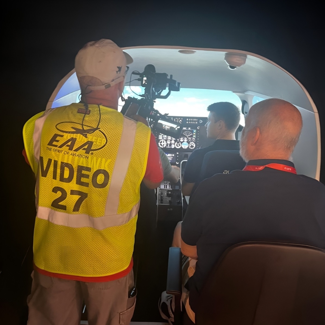 View from the back of an Alsim flight simulator with three people seated and one person filming