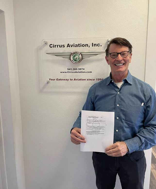 Student holding a certificate and smiling at the camera inside Cirrus Aviation's office