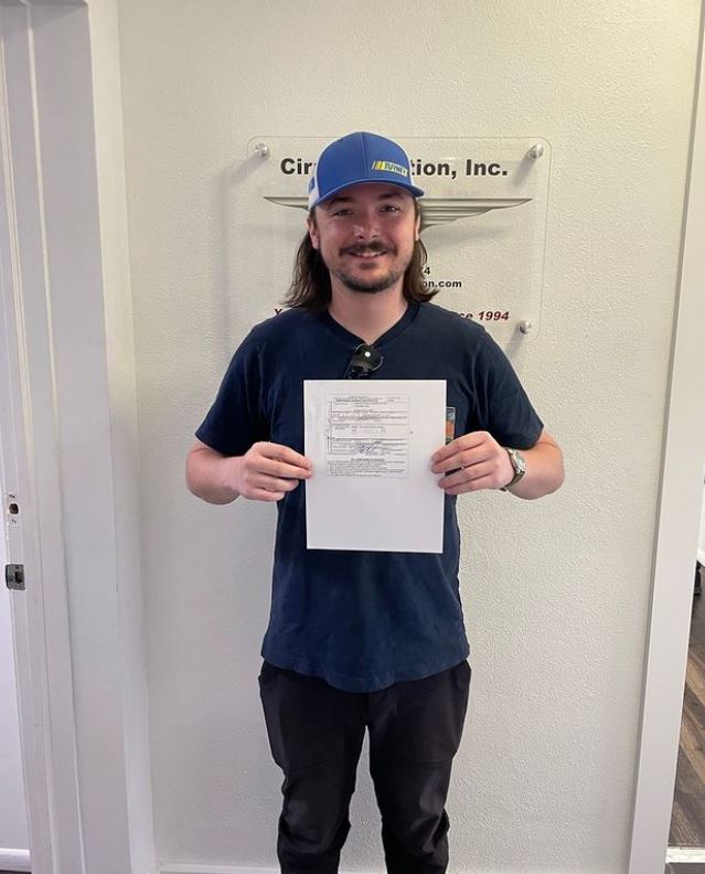 Student holding a certificate and smiling at the camera inside Cirrus Aviation's office