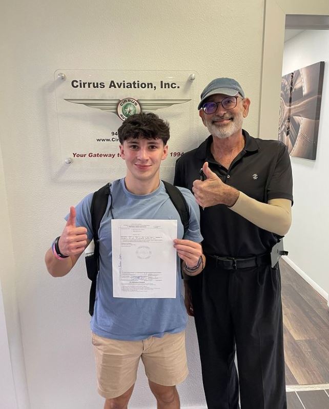 Student and man holding a certificate and smiling at the camera inside Cirrus Aviation's office