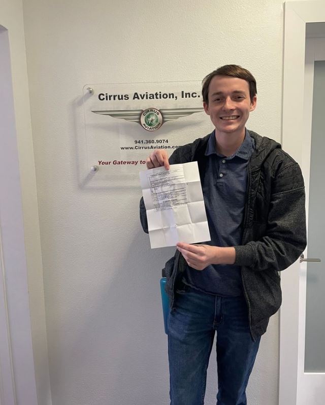Student holding a certificate and smiling at the camera inside Cirrus Aviation's office