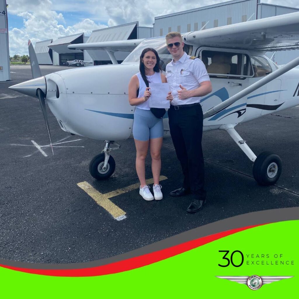 Student and CFI standing in front of a Cessna aircraft, Cirrus Aviation watermark at the bottom of the image