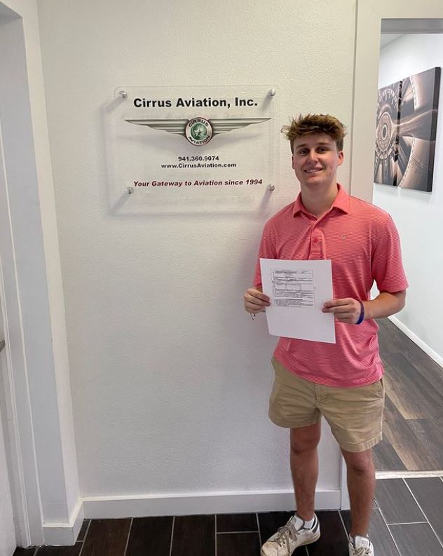 Student holding a certificate and smiling at the camera inside Cirrus Aviation's office