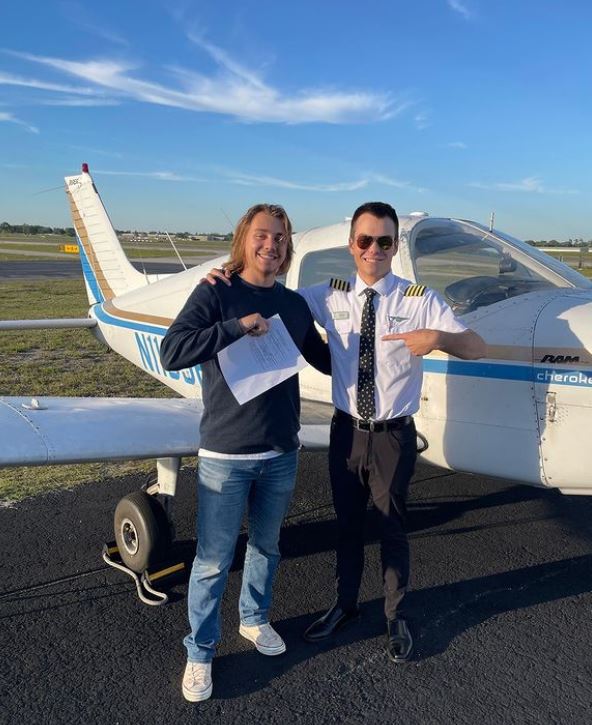 Student and CFI holding certificate in front of a Piper Warrior aircraft