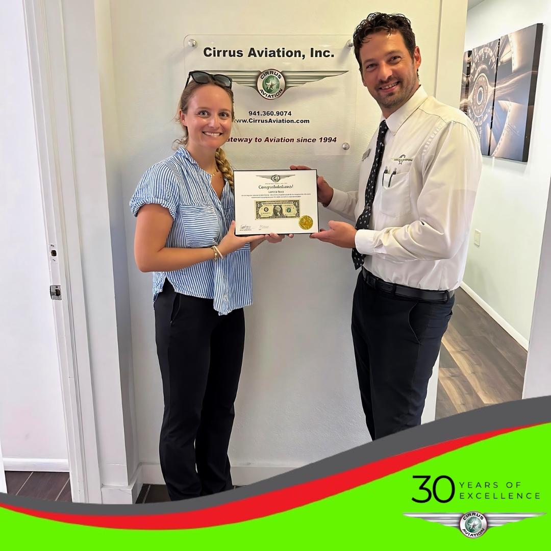 Student and CFI holding certificate and smiling at the camera, Cirrus Aviation watermark at the bottom of the image