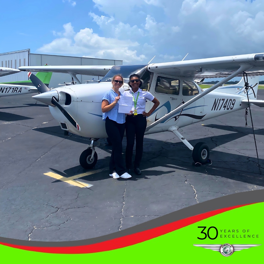 Student holding certificate with CFI in front of a Cessna aircraft, Cirrus Aviation watermark at the bottom of the image