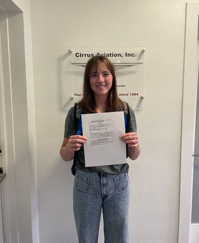 Student holding a certificate and smiling at the camera inside Cirrus Aviation's office