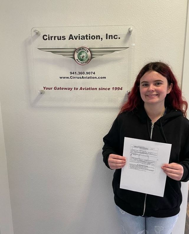 Student holding a certificate while smiling at the camera inside Cirrus Aviation's office