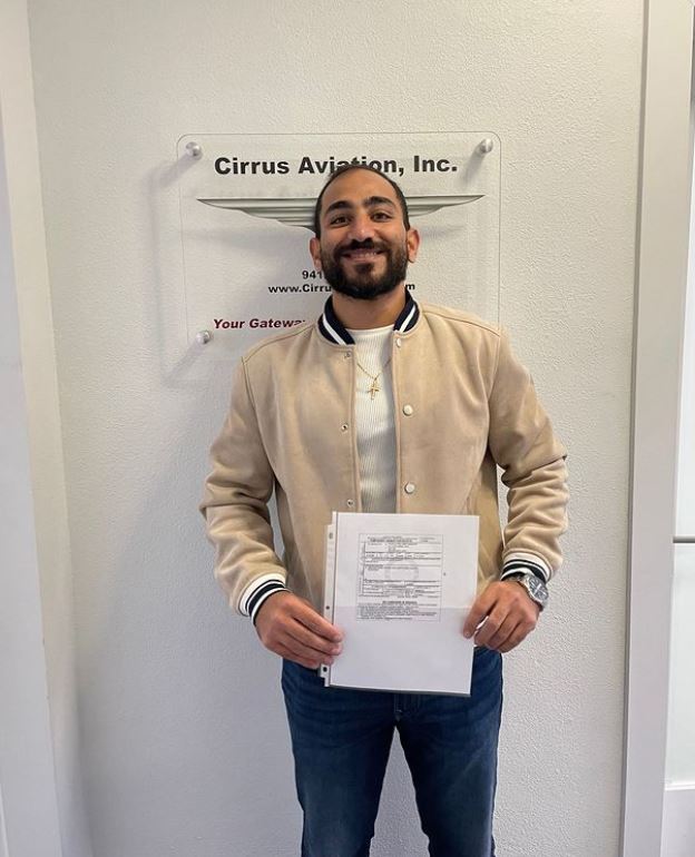 Student holding a certificate and smiling at the camera inside Cirrus Aviation's office
