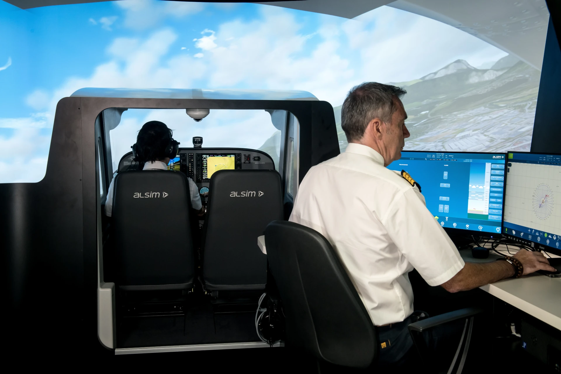 Flight simulator study session, man operating the simulator settings from outside while a pilot trains in inside