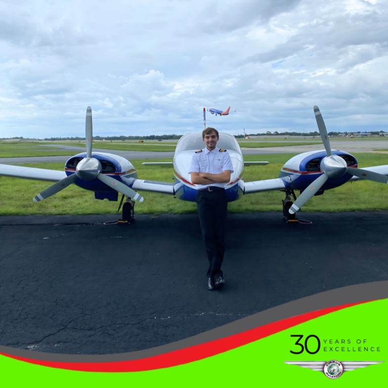 Pilot standing in front of an airplane with arms crossed. Cirrus Aviation logo in the bottom right