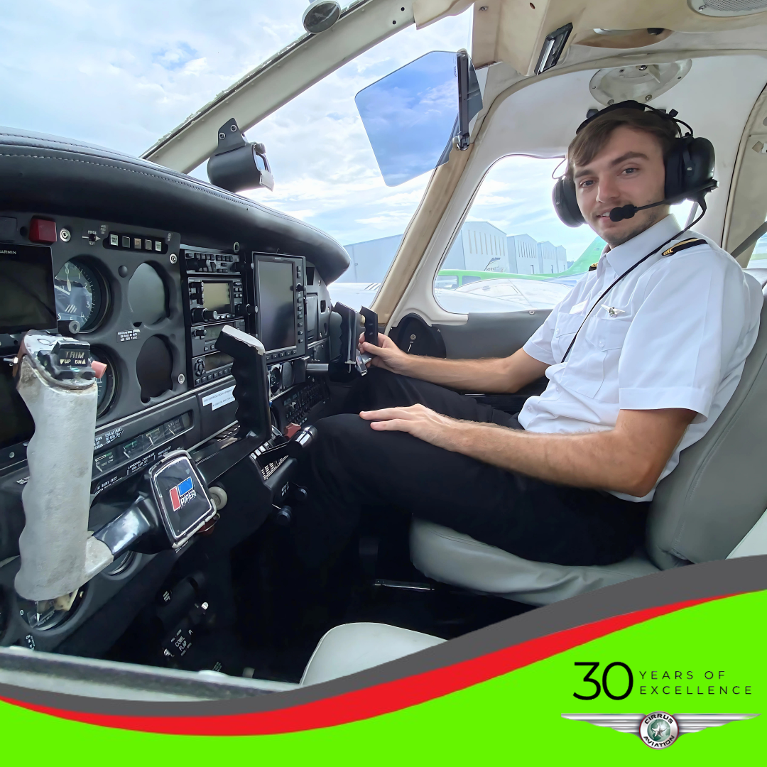 Pilot in the cockpit seen through the left open door of the plane. Cirrus Aviation logo in the bottom right