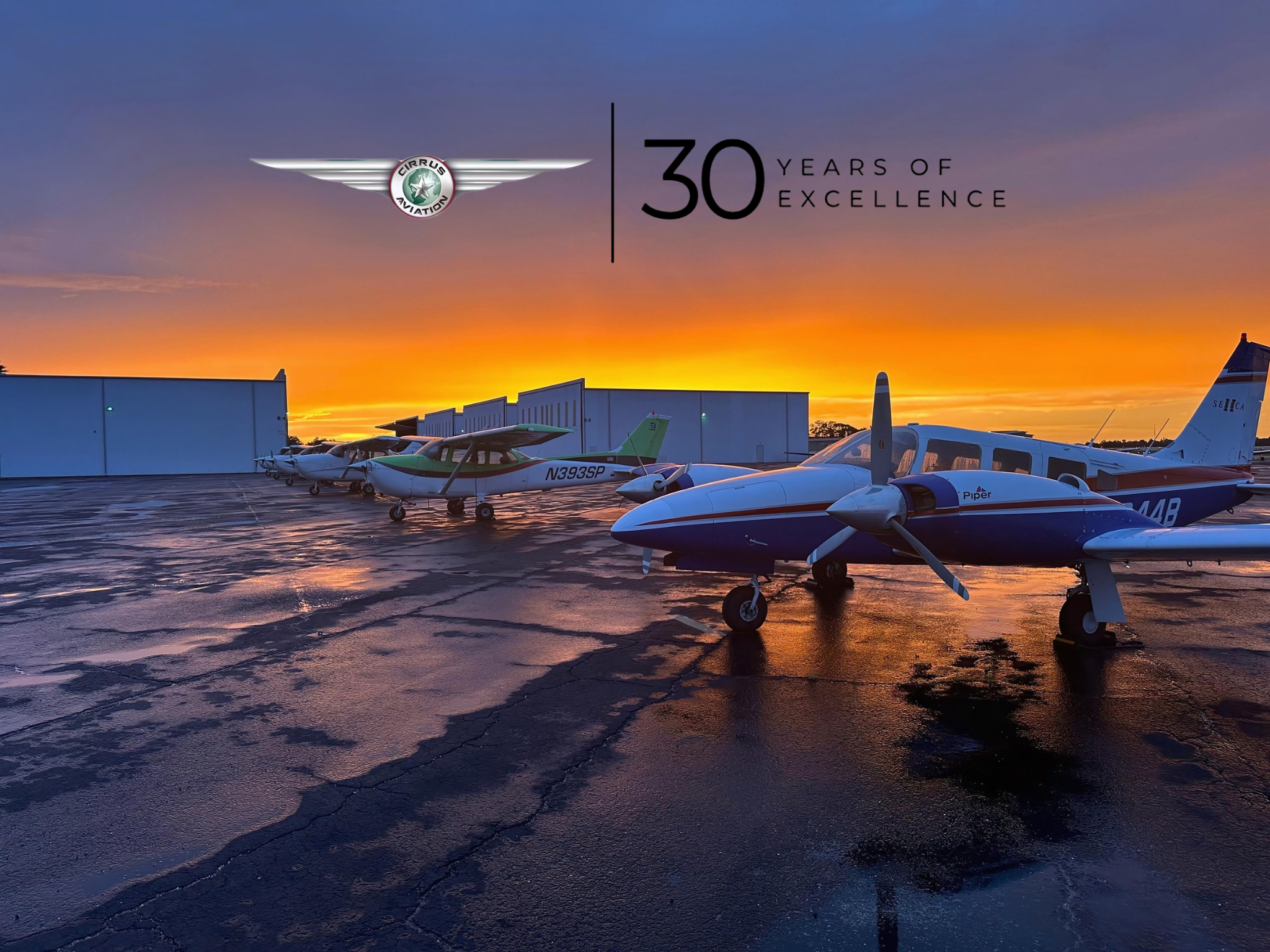 Airplanes lined up with the sunset and airplane hangars in the background